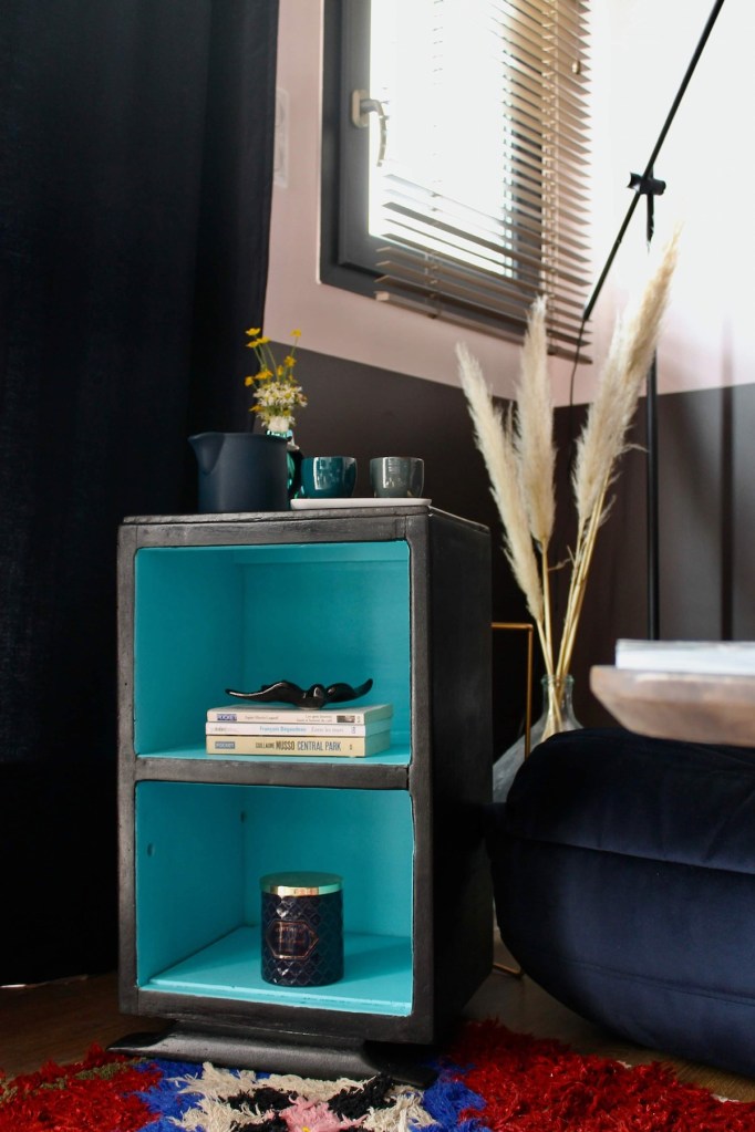 Meuble de rangement moderne avec une structure noire et un intérieur bleu, décoré avec des livres, un objet décoratif et une bougie, dans un intérieur contemporain.